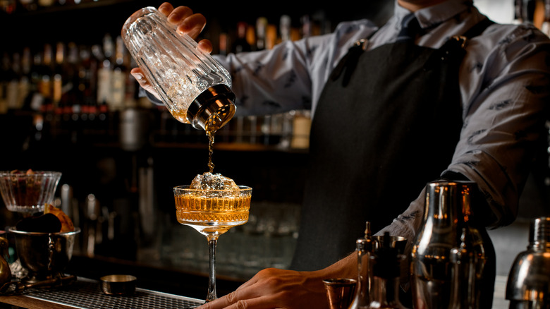 Professional,Bartender,In,Black,Apron,Pours,Brown,Alcoholic,Drink,From