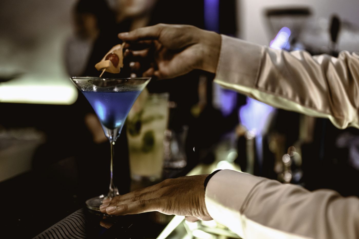 The young bartender is making a cocktail and decorating it in a martini cocktail glass for beautiful at a nightclub bar.